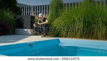 Technician working by the pool, checking a tablet while surrounded by greenery.