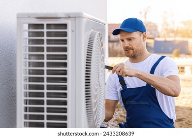 technician working on air conditioning or heat pump outdoor unit. HVAC service, maintenance and repair - Powered by Shutterstock