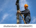 A technician working on ladder carefully for maintenance fiber optic wires attached to electric poles. Safety equipment and Operational safety.