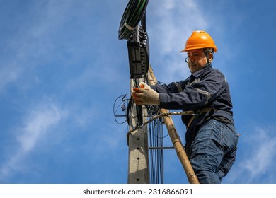 A technician working on ladder carefully for maintenance fiber optic wires attached to electric poles. Safety equipment and Operational safety. - Shutterstock ID 2316866091
