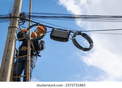 A technician working on ladder carefully for maintenance fiber optic wires attached to electric poles. Safety equipment and Operational safety. - Powered by Shutterstock