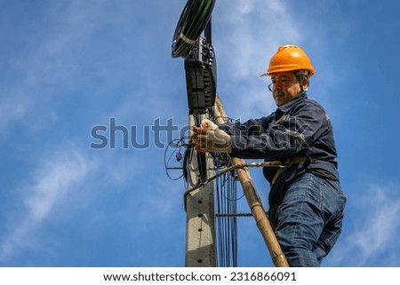 A technician working on ladder carefully for maintenance fiber optic wires attached to electric poles. Safety equipment and Operational safety.