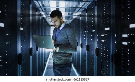 IT Technician Works on a Laptop in Big Data Center full of Rack Servers. He Runs Diagnostics and Maintenance, Sets up System. - Powered by Shutterstock