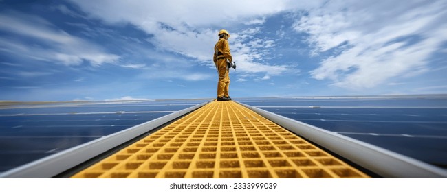 Technician Young Wearing Safety Protective Clothing on Walkway with Tool Standing to Checking Quality of Solar Panel or Photovoltaic Installation in Daytime on Factory Roof Buildings.