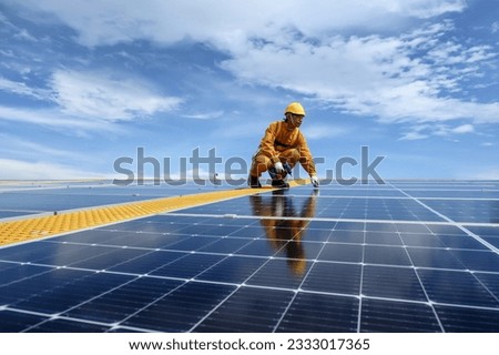 Technician Young Wearing Safety Protective Clothing with Installing Tool while Install Solar Panel or Photovoltaic in Daytime on Factory Roof Buildings.