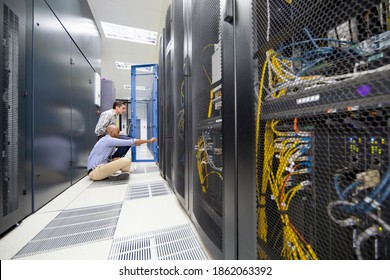 Technicians checking server in the data center hall using a laptop and a digital tablet
