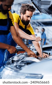 Technicians collaborating on servicing broken vehicle, checking for faulty ignition system. Meticulous repairmen in auto repair shop working together on fixing automobile, discussing best options