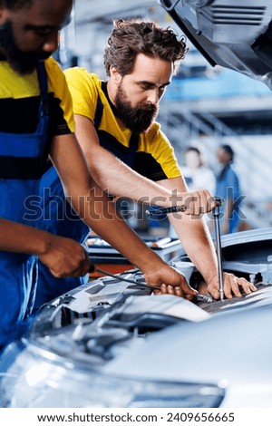 Technicians collaborating on servicing broken vehicle, checking for faulty ignition system. Meticulous repairmen in auto repair shop working together on fixing automobile, discussing best options
