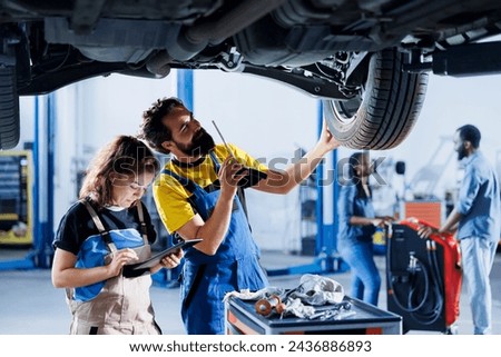 Technicians collaborating on servicing broken vehicle, checking for faulty wheels. Skillful repairmen in auto repair shop working together on fixing automobile, discussing best options