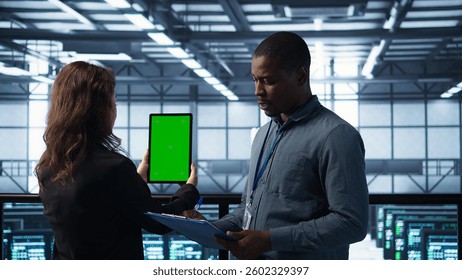 Technicians in data center using green screen tablet, reviewing hardware diagnostics. IT coworkers adjusting server configurations using mockup device, applying firmware updates, camera B