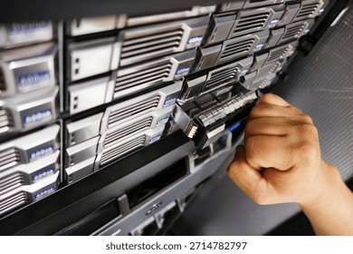 A technician's hand inserts a drive into a server rack unit in a modern data center, showcasing technology and efficient data management solutions.