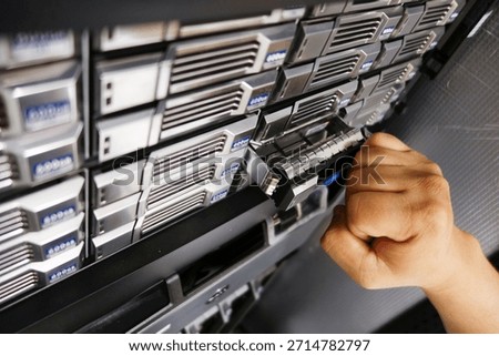 A technician's hand inserts a drive into a server rack unit in a modern data center, showcasing technology and efficient data management solutions.