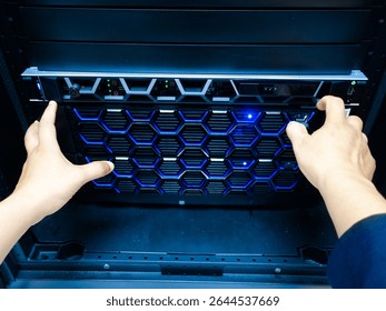 A technician's hands operate a modern server unit featuring blue LED lights. The image captures the intricacies of technology in a professional IT environment.