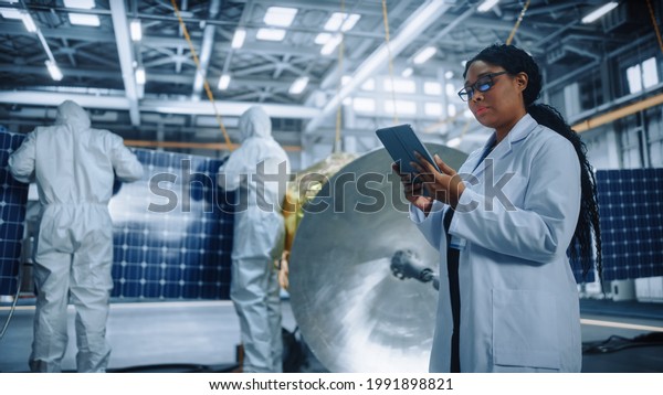 Technicians in Protective Suits Working on\
Satellite Construction, under Chief Engineer Control. Aerospace\
Agency: Team of Scientists Fixing Solar Panel Wings to Spacecraft.\
Space Exploration\
Mission