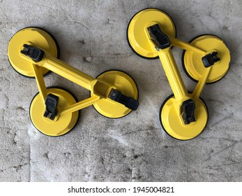 A technician's tool with glass expertise called a glass sucker to lift. 3 legs glass sucker painted in yellow. A top-down look of two yellow glass suckers placed on an old foam floor.
