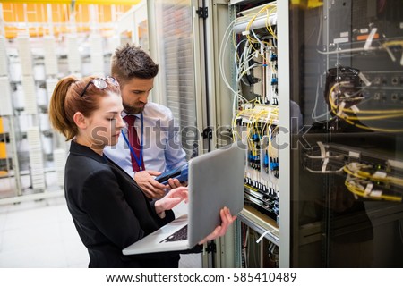 Technicians using laptop while analyzing server in server room