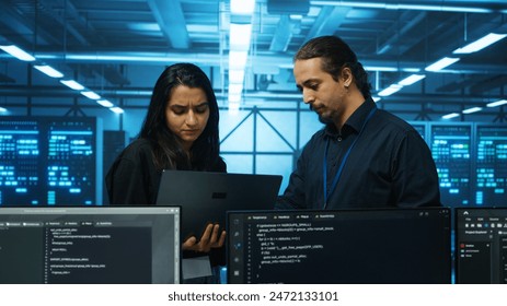 Technicians working in high tech server hub, analyzing data on laptop to ensure seamless data flow. Coworkers examining equipment in data center, ensuring system integrity and security