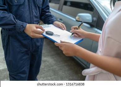 Technicisn Repairman Giving Car Key To Woman.
Workshop Mechanic Repair Client Car In Auto Service Shop. 
Female Customer Sign Paper Insurance Bill Contact In Garage. Fixing Car Concept.