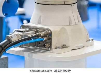 Technological component with robotic bracket, white cylindrical body mounted on platform, metallic ports and connectors, blue hose and black cable, secure assembly with screws, clean indoor setting