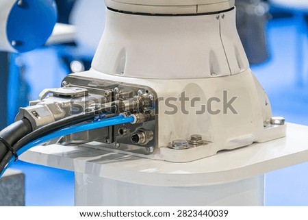 Technological component with robotic bracket, white cylindrical body mounted on platform, metallic ports and connectors, blue hose and black cable, secure assembly with screws, clean indoor setting