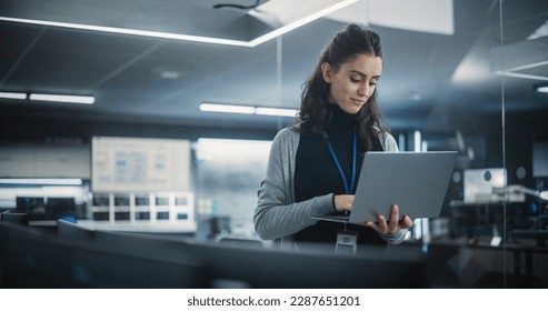 Technological Software Engineering Department Manager Standing and Using a Laptop Computer. Multiethnic Female Looking in the Distance and Thinking while Working in the Office - Powered by Shutterstock