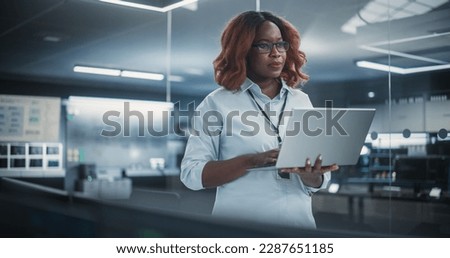 Technological Software Engineering Department Manager Standing and Using a Laptop Computer. Black Female Looking in the Distance and Thinking while Working in the Office