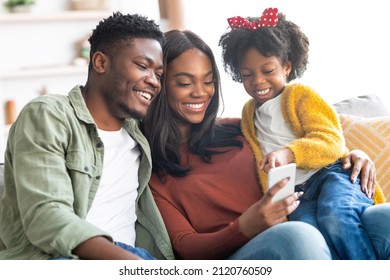 Technologies For Leisure. Black Family Of Three Using Smartphone At Home Together, Happy Young African American Parents And Little Daughter Relaxing On Couch With Mobile Phone, Closeup Shot