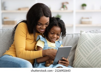 Technologies For Leisure. Happy Black Mother And Little Daughter Using Digital Tablet Together While Sitting On Couch At Home, African American Mom And Female Child Shopping Online With Modern Gadget