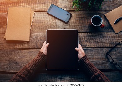 Technologies make life easier. Close-up top view image of woman holding digital tablet with copy space while sitting at the rough wooden table  - Powered by Shutterstock