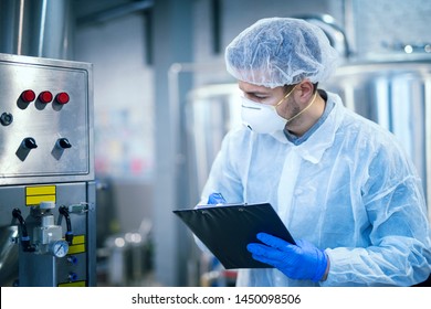 Technologist Expert In Protective Uniform With Hairnet And Mask Taking Parameters From Industrial Machine In Food Production Plant.