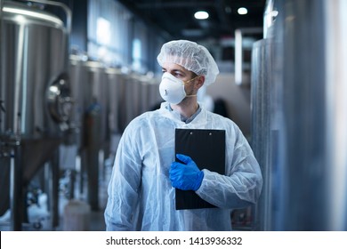 Technologist in protective white suit with hairnet and mask standing in food factory. - Powered by Shutterstock