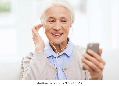 Technology, Age And People Concept - Happy Senior Woman With Smartphone And Earphones Listening To Music At Home