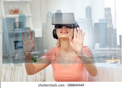technology, augmented reality and entertainment concept - happy young woman in virtual headset 3d glasses and headphones playing game at home with singapore city skyscrapers on screen projection