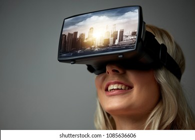 technology, augmented reality, entertainment and people concept - happy young woman with virtual headset or 3d glasses playing video game with singapore city on screen over gray background