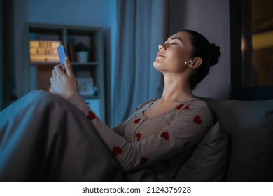 technology, bedtime and people concept - happy teenage girl with smartphone and earphones enjoying music sitting in bed at home at night - Powered by Shutterstock