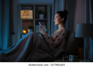 technology, bedtime and people concept - happy smiling teenage girl with smartphone and earphones sitting in bed at home at night - Powered by Shutterstock