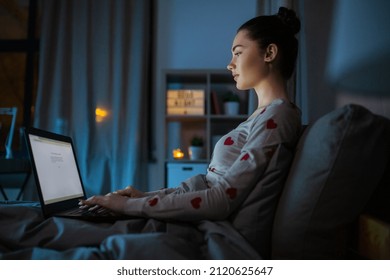 technology, bedtime and people concept - teenage girl with laptop computer sitting in bed at home at night - Shutterstock ID 2120625647