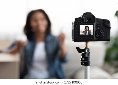 Technology and blogging concept. African woman recording video concent for her beauty blog at home, selective focus on camera with preview screen