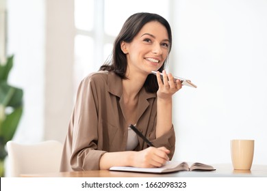 Technology And Communication Concept. Happy Woman Using Voice Command Recorder On Mobile Phone And Taking Notes