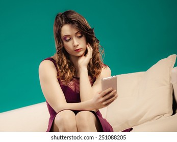 Technology And Communication. Elegant Young Woman Sitting On Couch Using Mobile Phone Texting Or Reading Sms. Bad News Unhappy Expression. Indoor