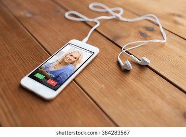 technology, communication, gadget and object concept - close up of white smartphone and earphones on wooden surface with incoming call on screen