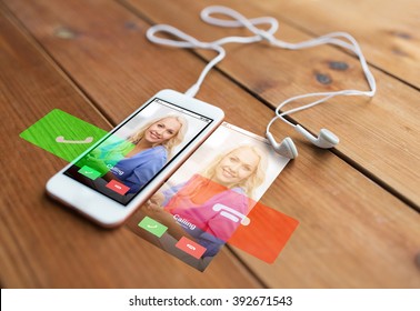 technology, communication, gadget and object concept - close up of white smartphone and earphones on wooden surface with incoming call on screen