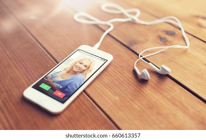 technology, communication, gadget and object concept - close up of white smartphone and earphones on wooden surface with incoming call on screen