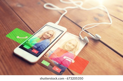 technology, communication, gadget and object concept - close up of white smartphone and earphones on wooden surface with incoming call on screen