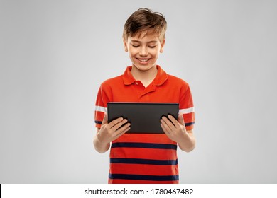 technology, communication and people concept - happy smiling boy in red polo t-shirt using tablet pc computer over grey background
