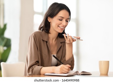 Technology, Communication And People Concept. Smiling girl using voice command recorder on smartphone and writing notes - Powered by Shutterstock