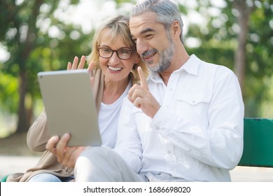 Technology Connect And Modern Elderly Lifestyles Concept. Aged Senior Couple Waving Hands Greeting Grandkids Via Facetime Video Call Internet Conference Outdoors In The Park