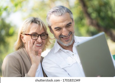 Technology connect and modern elderly lifestyles concept. Aged senior couple waving hands greeting grandkids via facetime video call internet conference outdoors in the park