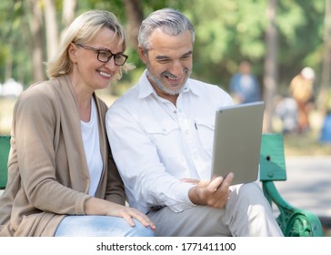 Technology Connect And Modern Elderly Lifestyles Concept. Aged Senior Couple Waving Hands Greeting Grandkids Via Facetime Video Call Internet Conference Outdoors In The Park