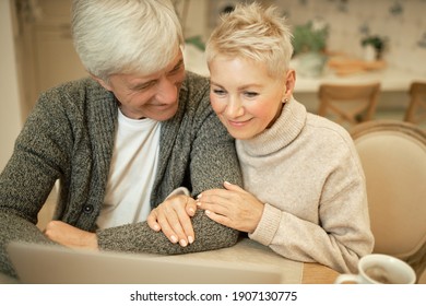 Technology, Connection, Leisure And Relationships. High Angle View Of Attractive Middle Aged Woman Embracing Her Cheerful Husband, Enjoying Series Via Online Streaming Service Using Laptop